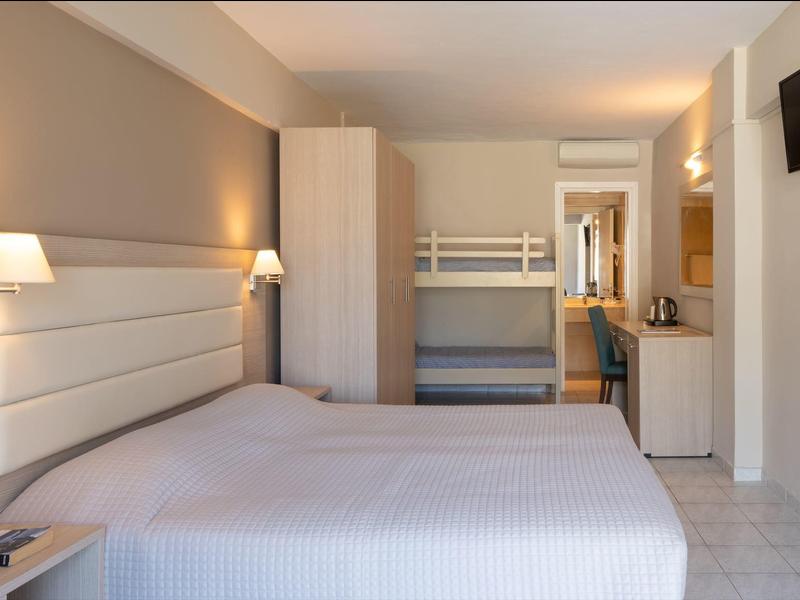 Chambre lumineuse avec lit double, lits superposés et télévision murale dans un hébergement hôtelier.