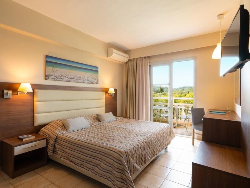 Chambre d'hôtel lumineuse avec lit double, TV, bureau et balcon avec vue sur le paysage.