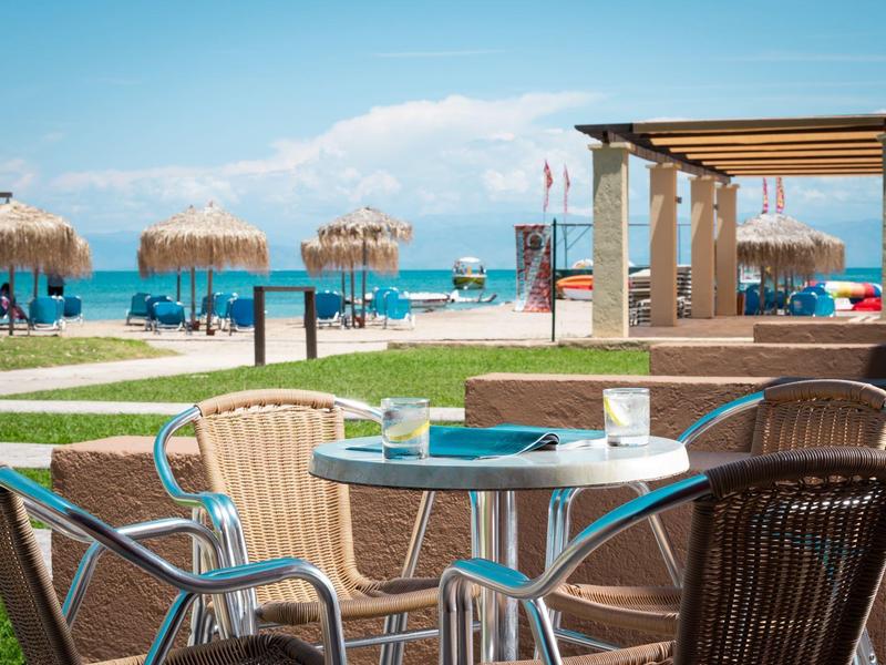 Café de plage avec chaises et tables, vue sur la mer et parasols en arrière-plan.