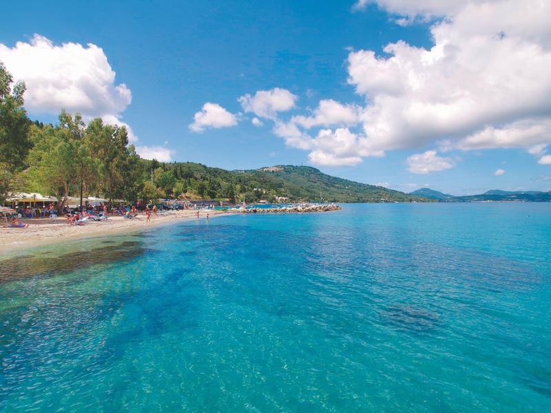 Klarer blauer Meerblick mit grünem Ufer, bewaldeten Hügeln und teilweise bewölktem Himmel.