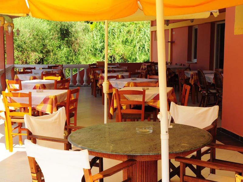 Terrasse mit Holztischen und Stühlen, gelbe Sonnenschirme und rotes Gebäude im Hintergrund.