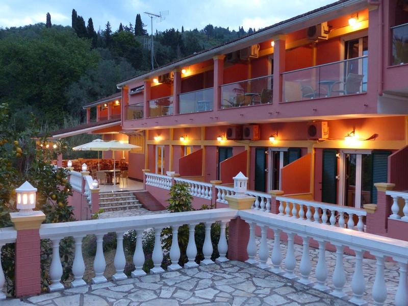 Beleuchtetes zweistöckiges Hotel mit Balkon und weißen Balustraden bei Dämmerung, umgeben von Hügeln.