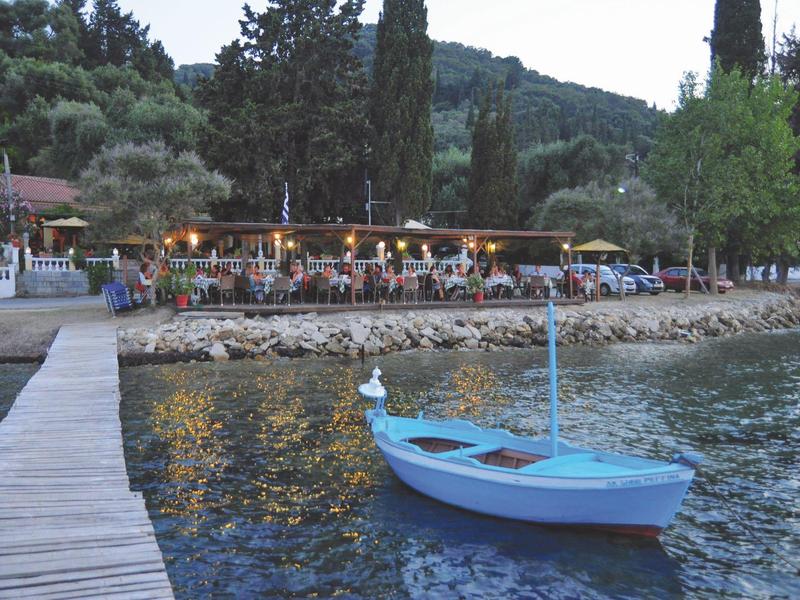 Blaues Boot auf ruhigem Wasser neben Holzsteg, gemütliches Restaurant mit Beleuchtung am Ufer.