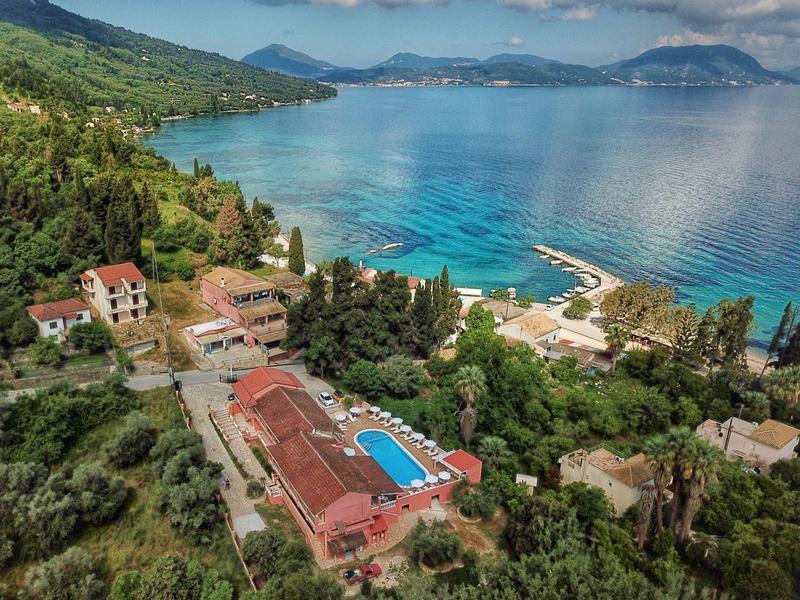 Luftaufnahme eines Küstenresorts mit blauem Pool, grünen Bäumen und klarem, türkisfarbenem Meer.