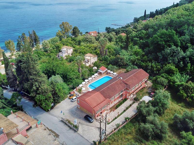Hotel mit rotem Dach, blauem Pool und viel Grün, nahe Küste und Meer.