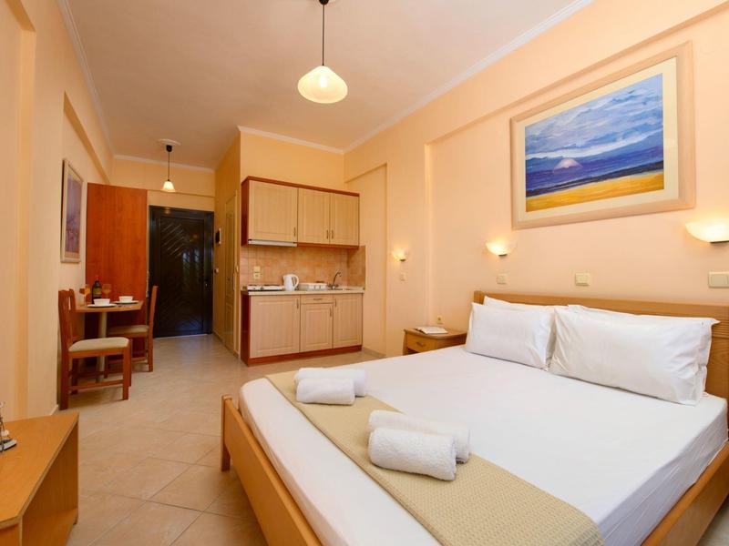 Helles Hotelzimmer mit Doppelbett, Holzmöbeln, Küchenzeile und Landschaftsgemälde an der Wand.