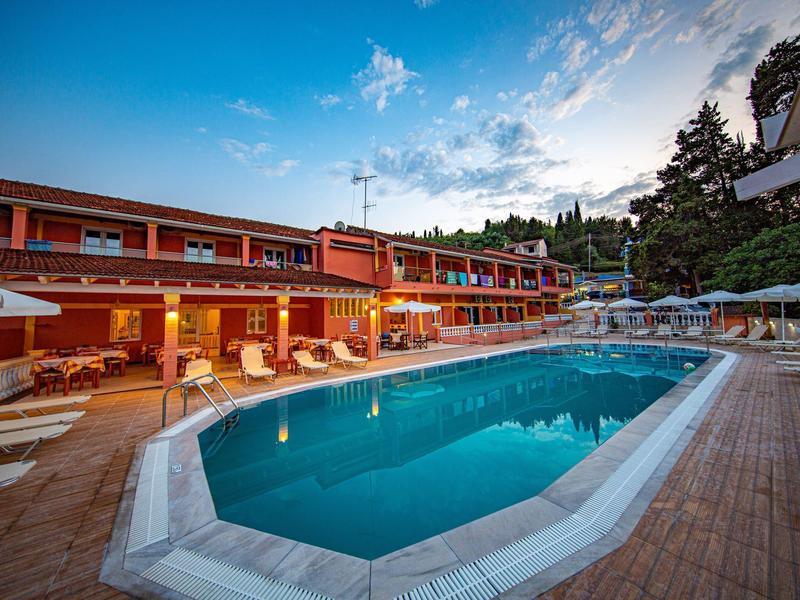 Moderner Außenpool mit blauen Wasser, umgeben von Holzdeck und roten Gebäuden im Abendlicht.