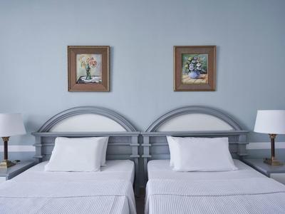 Twin beds with white linens, gray headboards, matching lamps, and wall art in a hotel room.