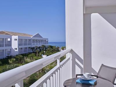 Balcony with table, chair, cup, and ocean view beside white buildings under clear blue sky.