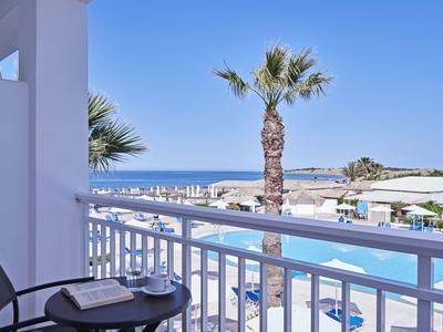 Balcony overlooking pool, palm tree, and ocean under clear blue sky at a resort.