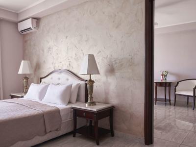 Elegant hotel room with beige walls, two lamps, and separate seating area with table and chairs.