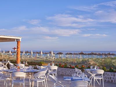 Terrace of a beachside restaurant with white chairs and tables overlooking the sea and sky.
