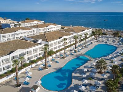 Large hotel with multiple pools and sun loungers next to the sea under a blue sky.