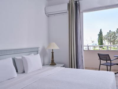 Bright hotel room with white bedding, bedside lamp, and balcony with table and chairs.