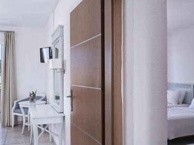 Modern hotel room with white furniture, a balcony, and a bed partially visible behind a wall.