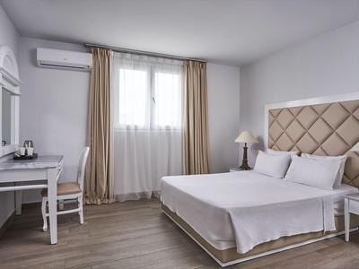 Bright hotel room with double bed, desk, chair, TV, and curtained window.