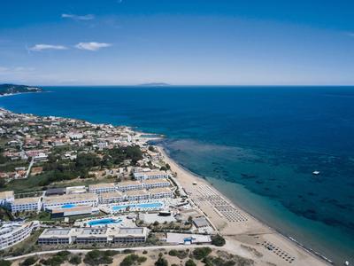 Coastal resort with sandy beaches, clear blue sea, and buildings along the shoreline under a sunny sky.