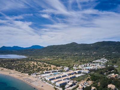 Coastal resort with sandy beach, white buildings, and green hills under a cloudy sky.