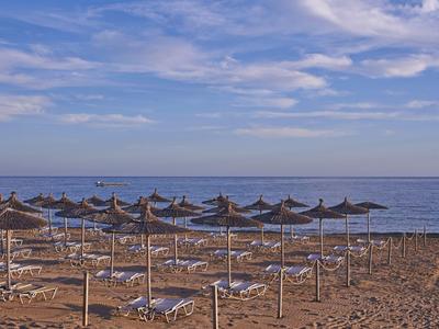 Empty beach with sun loungers and umbrellas by calm sea under cloudy sky