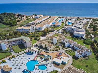 Aerial view of a coastal resort with multiple buildings, pools, and greenery near the ocean.