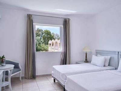 Bright hotel room with two single beds, white walls, and a window overlooking trees.