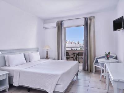 Bright hotel room with white decor, double bed, desk, and balcony with a sea view.