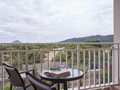 Balcony with table, two chairs, and a view of greenery and mountains under a cloudy sky.