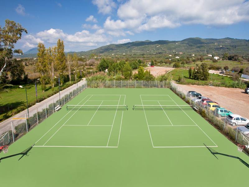 Outdoor tennis courts with clear skies and parked cars along the side near a rural landscape.