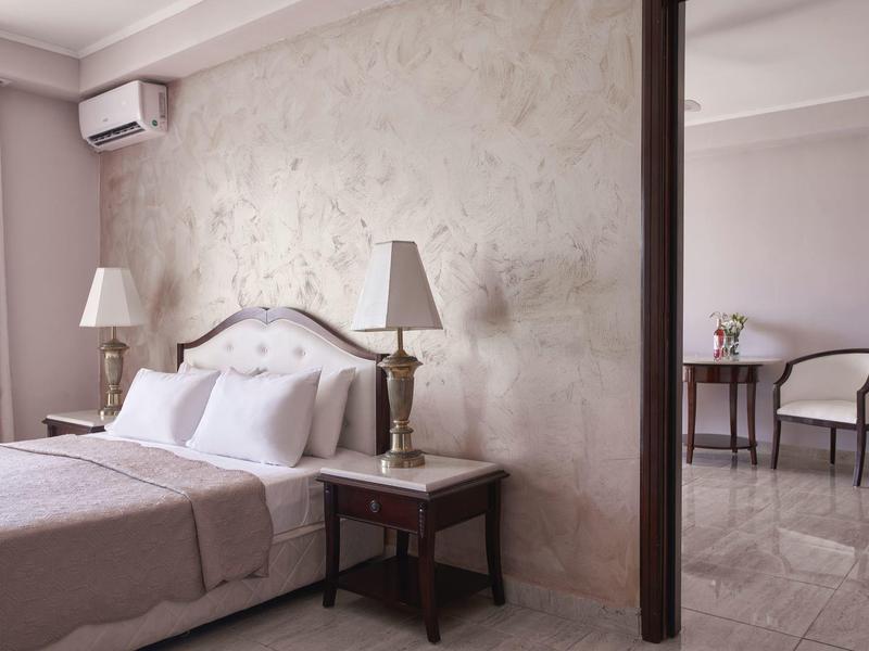 Elegant hotel room with beige walls, two lamps, and separate seating area with table and chairs.