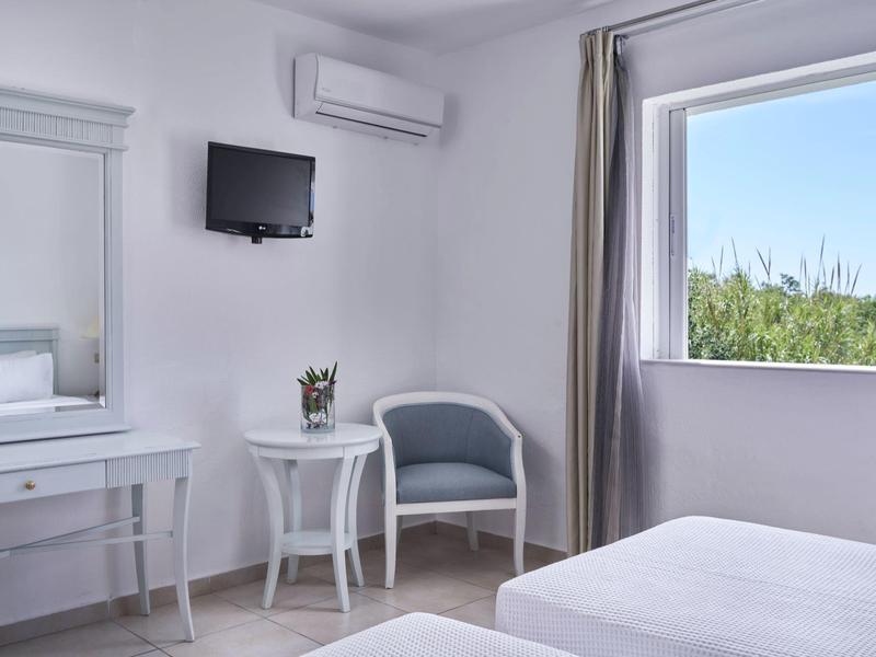 Bright hotel room with twin beds, a mirror desk, small table with chair, and a large window showing greenery.
