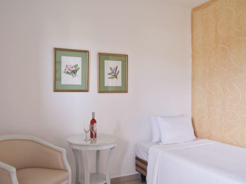 Cozy hotel room with single bed, beige chair, round table, and wall art by a wooden panel.
