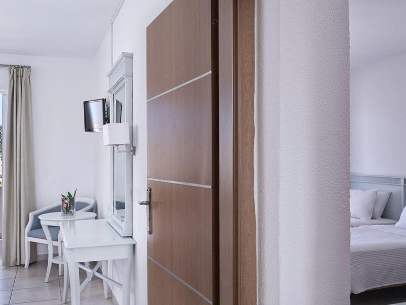 Modern hotel room with white furniture, a balcony, and a bed partially visible behind a wall.