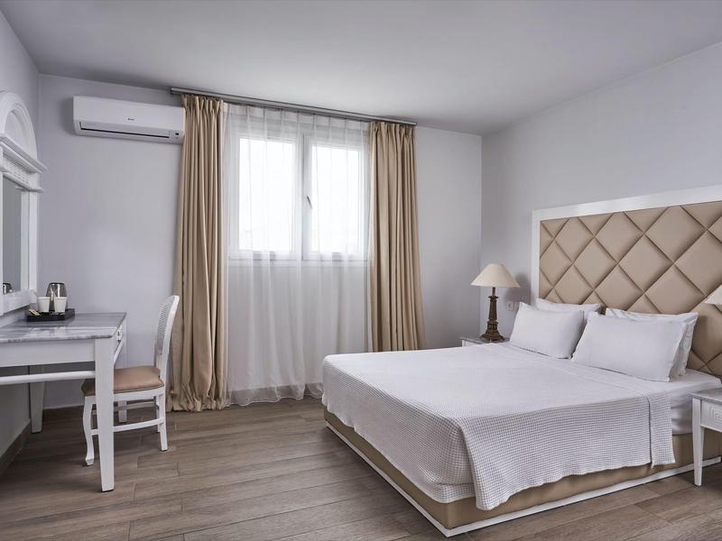 Bright hotel room with double bed, desk, chair, TV, and curtained window.