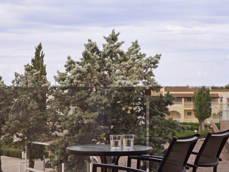 Balcony with table, two chairs, and trees with a building in the background.