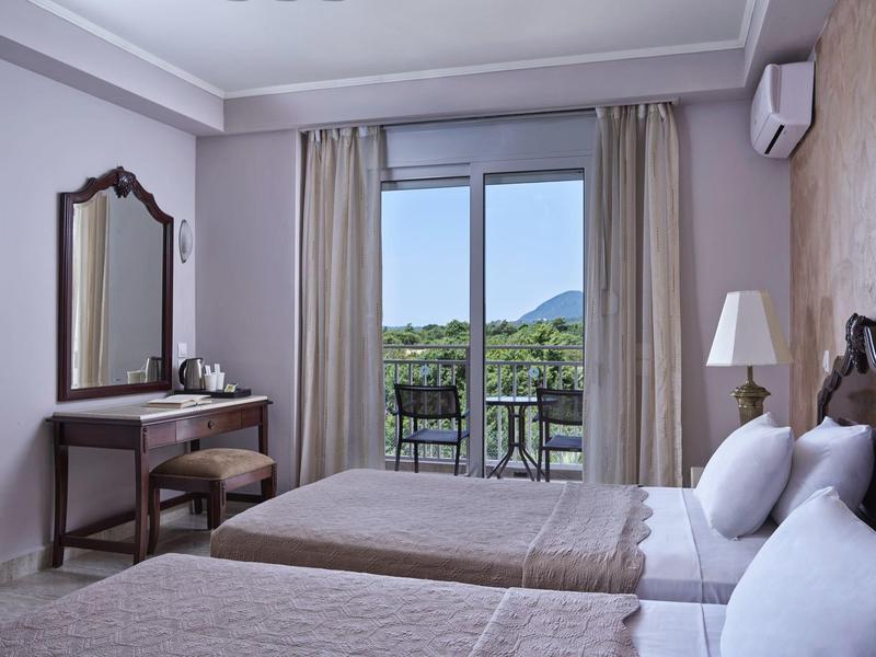 Hotel room with two beds, a desk, and a balcony overlooking greenery and hills.
