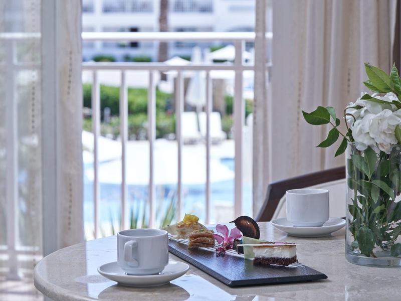 Table with coffee cups, flowers, and pastries near a window with a pool view.