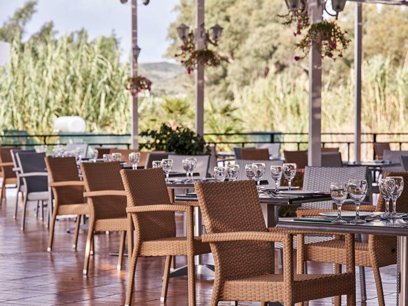 Outdoor dining area with wooden tables and woven chairs surrounded by greenery.