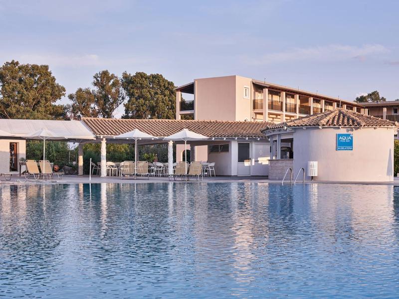 Large outdoor pool with a adjacent white pool bar and hotel building in the background.