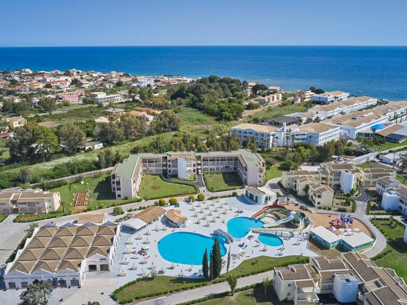 Aerial view of a coastal resort with swimming pools, hotels, and ocean in the background.