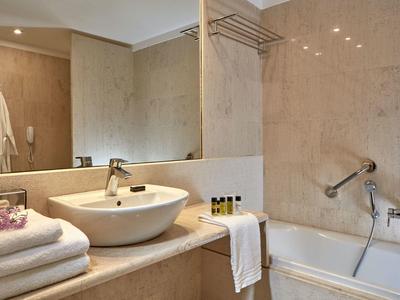 Modernes Badezimmer mit beige Marmor, weißem Waschbecken und Badewanne mit Handtüchern und Pflegeprodukten.