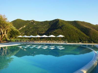 Infinity-Pool mit Liegestühlen vor grünen Hügeln und klarem blauem Himmel.