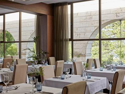 Helles Restaurant mit großen Fenstern, weißen Tischdecken und gemütlichen Stühlen in warmen Tönen.