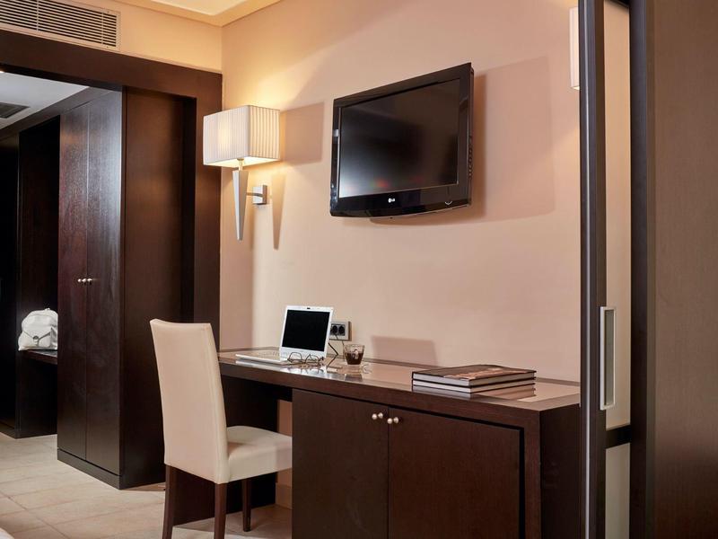 Moderner Arbeitsbereich mit weißem Stuhl, Laptop, Bücher auf dunklem Holztisch und Wandfernseher.