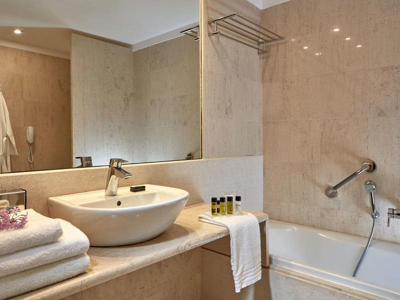 Modernes Badezimmer mit beige Marmor, weißem Waschbecken und Badewanne mit Handtüchern und Pflegeprodukten.