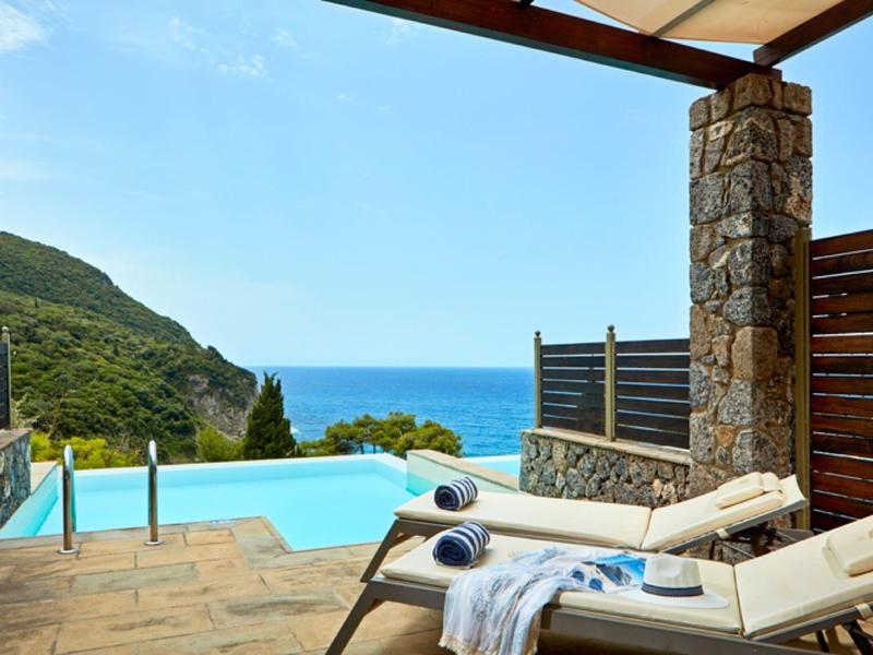 Terrasse mit Pool, zwei Liegen mit Handtüchern, Blick auf grünen Hügel und blaues Meer.