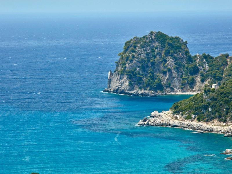 Klarblaue Küste mit felsigem, bewachsenem Kap und klarem, türkisfarbenem Wasser.