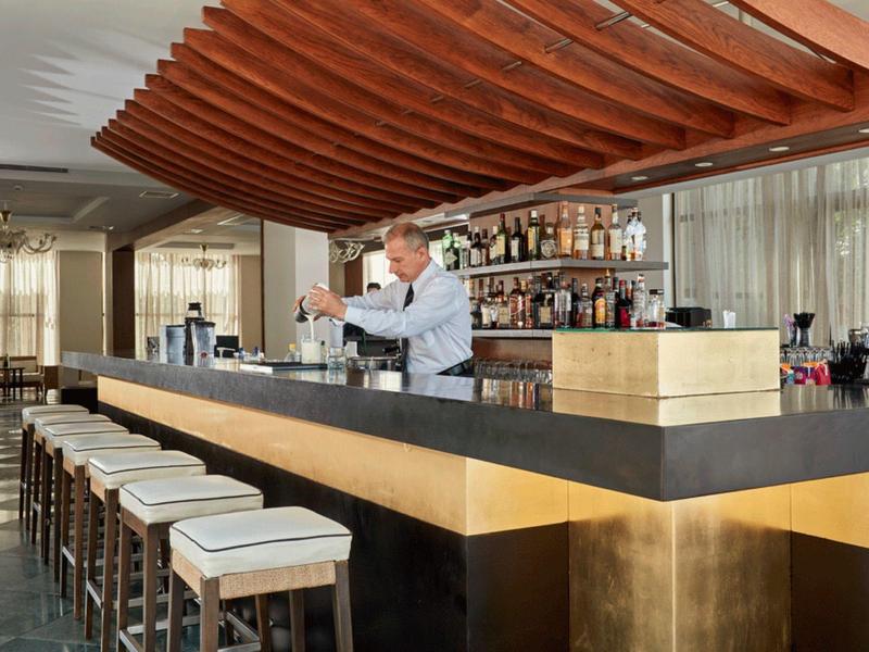 Moderner Barbereich mit dunkler Theke, goldfarbenen Akzenten und hölzernen Deckenlamellen.