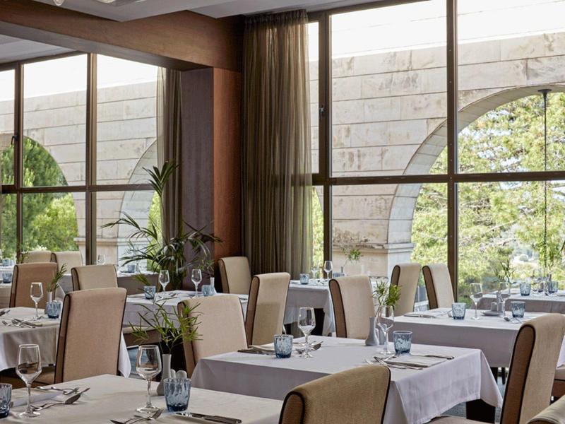 Helles Restaurant mit großen Fenstern, weißen Tischdecken und gemütlichen Stühlen in warmen Tönen.