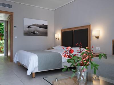 Helles Schlafzimmer mit Doppelbett, grauer Bettwäsche, Pflanzen und offenem Blick auf einen Garten.