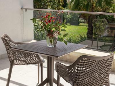 Moderner Balkon mit grauem Tisch, zwei geflochtenen Stühlen und Blumenstrauß im Glasvase.